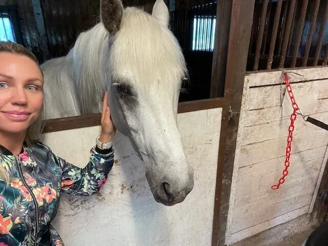 Pia med en vit häst i ett stall